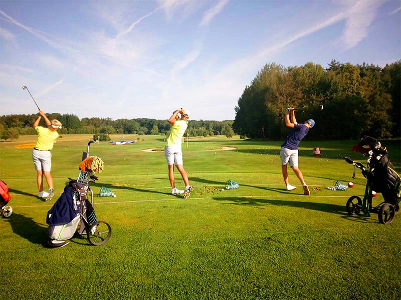 Drei jugendliche Golfer beim Abschlagen auf der Driving-Range